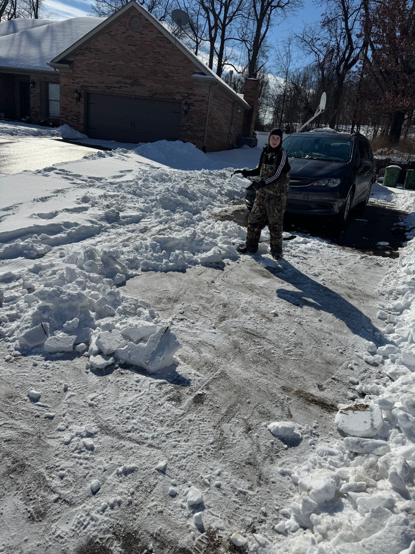Jase shoveling a snow-covered driveway beside a brick house after a heavy snowfall