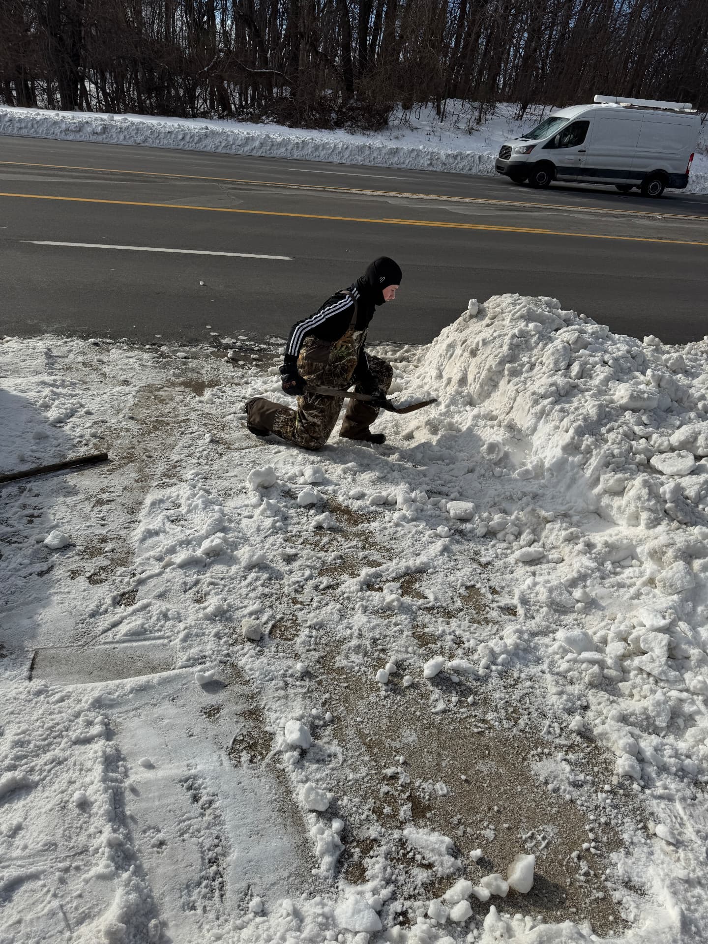 Jase clearing packed snow from a parking area along a road in freezing weather